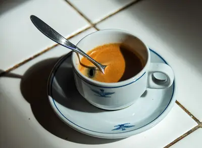 Chávena de café expresso acabado de tirar, com uma colher, ao sol numa bancada de cozinha