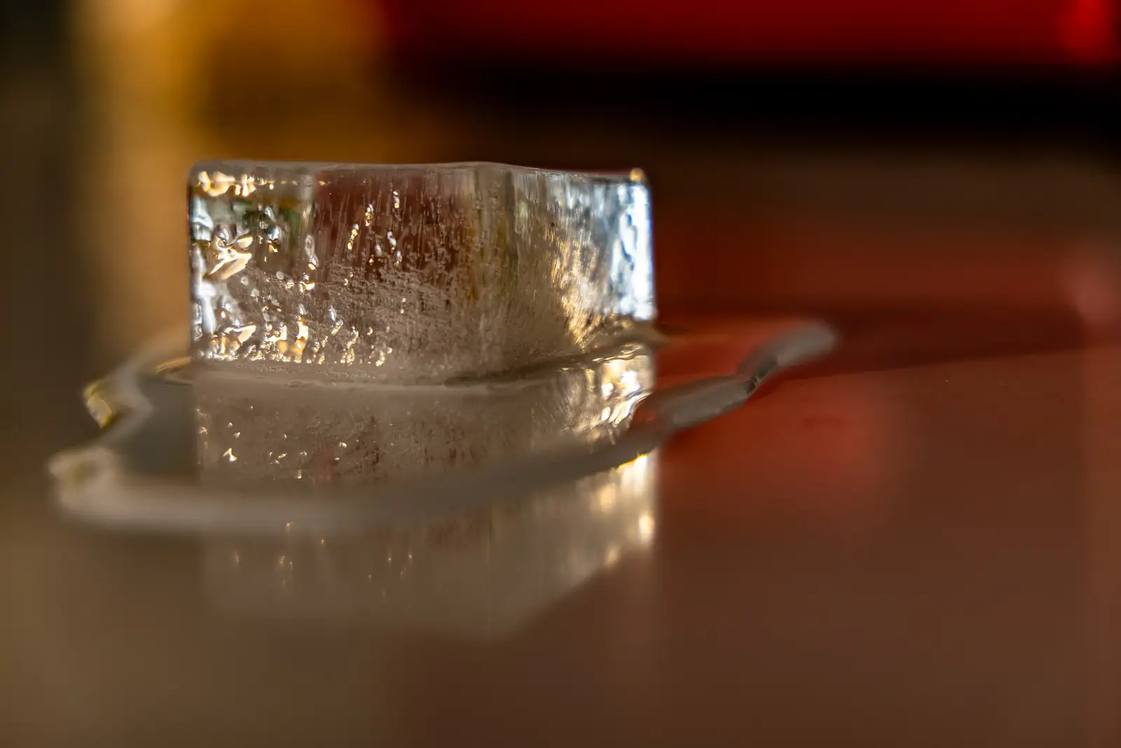 Um cubo de gelo a derreter numa poça de água sobre uma mesa