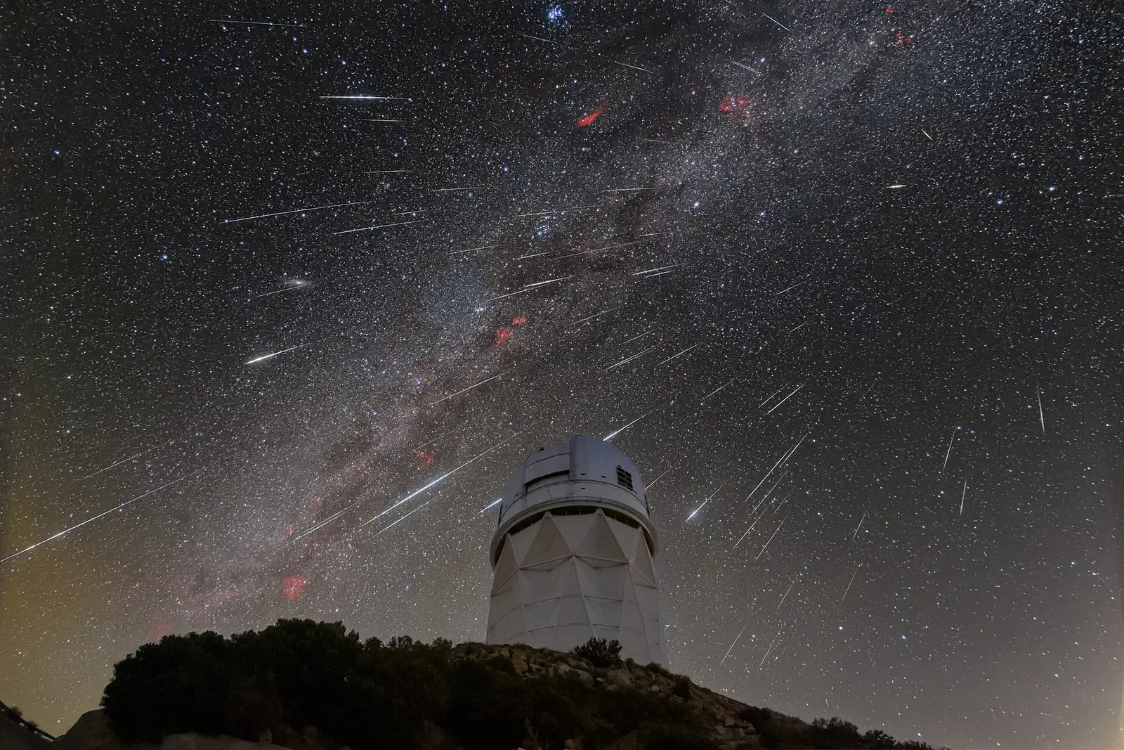 Dezenas de riscos de meteoros das Gemínidas no céu estrelado, sobre a cúpula de um observatório