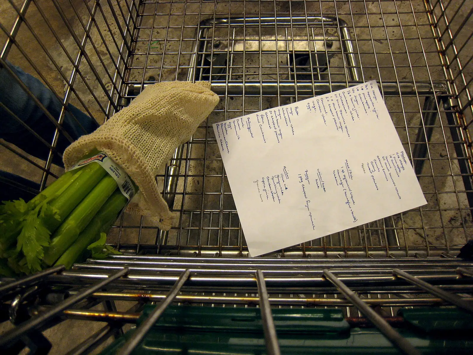 Lista de compras escrita à mão dentro de um carrinho de supermercado, ao lado de aipo