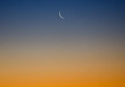 Lua em crescente fino no céu do crepúsculo, entre o azul e o laranja