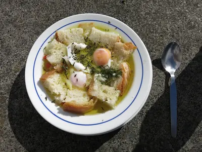 Prato de açorda com pedaços de pão, ovos escalfados, azeite e ervas