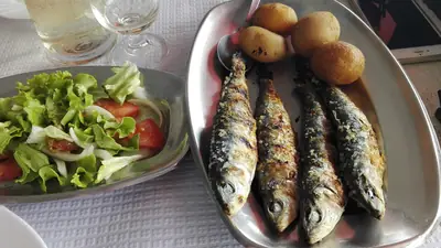 Travessa de sardinhas assadas com batatas, ao lado de uma taça de salada